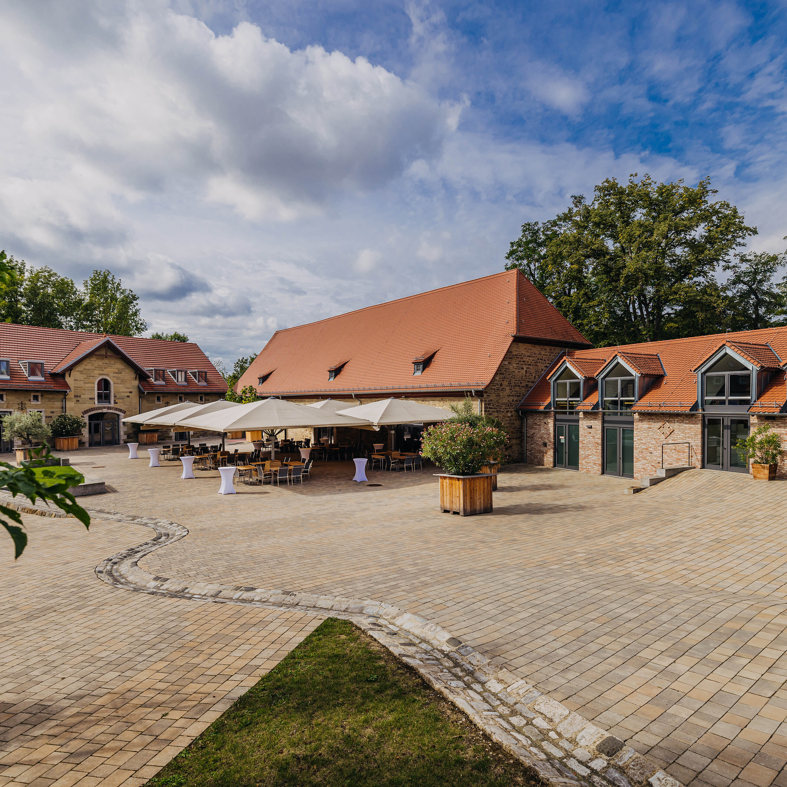 Große Festscheune und weitläufiger Innenhof der Eventlocation Gut Wöllried in Würzburg mit Sonnenschirmen für ein Sommerevent
