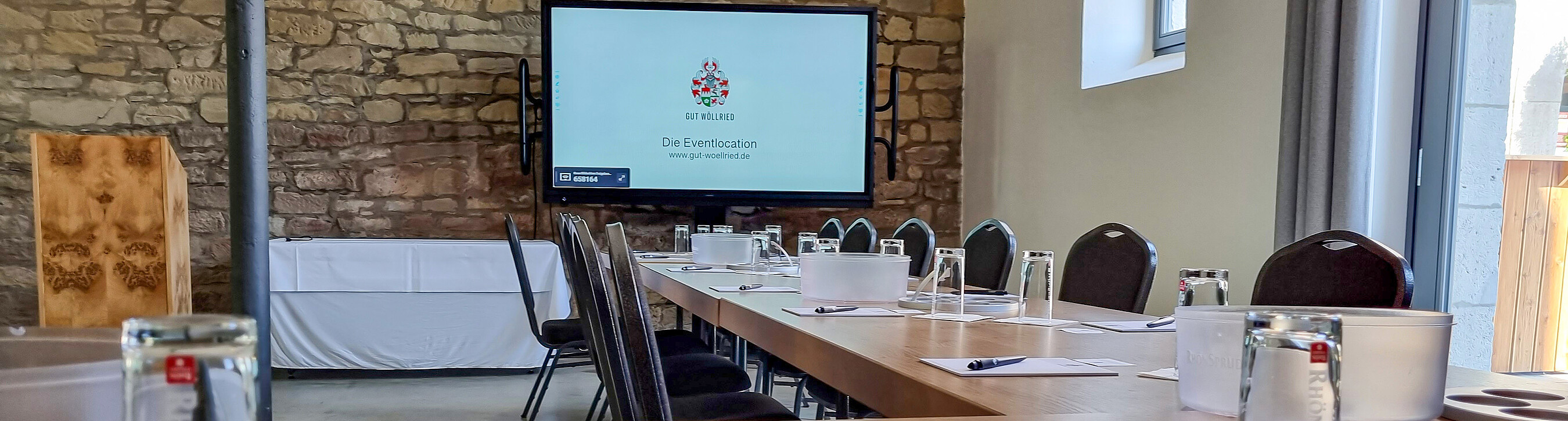 Großer Fernseher mit Logo der Eventlocation Gut Wöllried und Bestuhlung in U-Form für ein Firmenevent im Alten Speicher