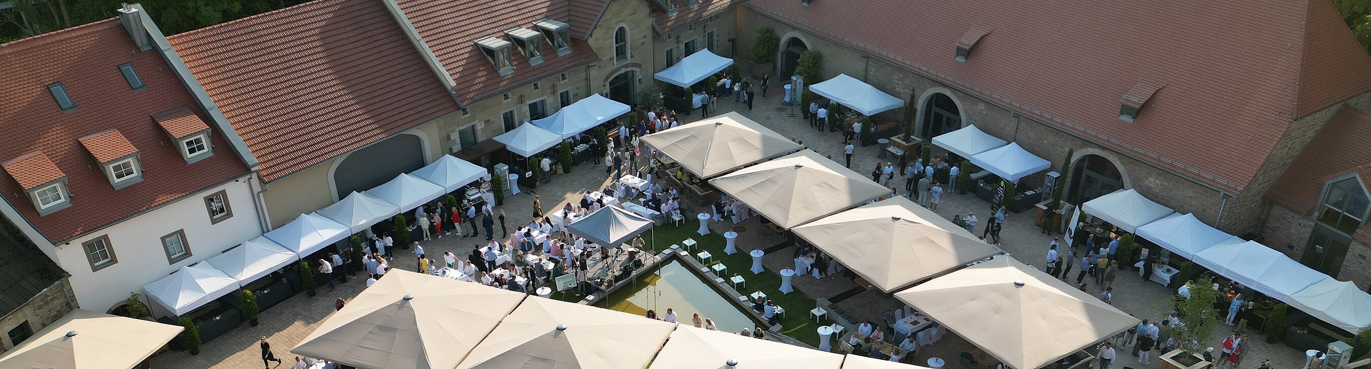 Viele Gäste, Sonnenschirme und Catering-Stände bei einer Veranstaltung im großen Außenbereich des Gutshofs "Gut Wöllried" 