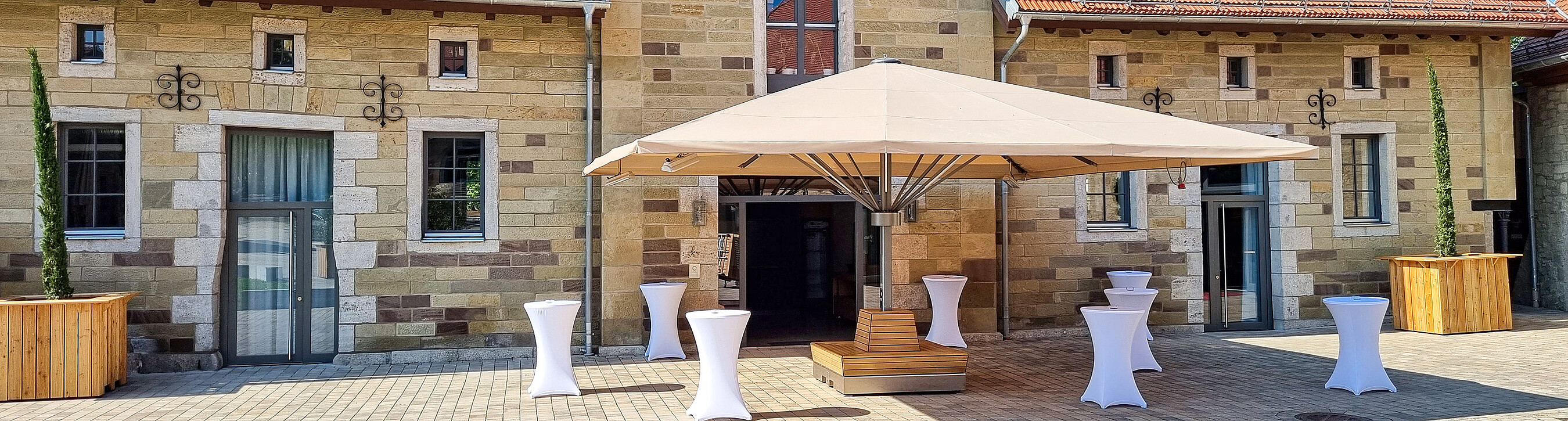 Alter Speicher mit Sonnenschirm und Cocktailtischen für einen Sektempfang bei einem Event im Sommer auf Gut Wöllried