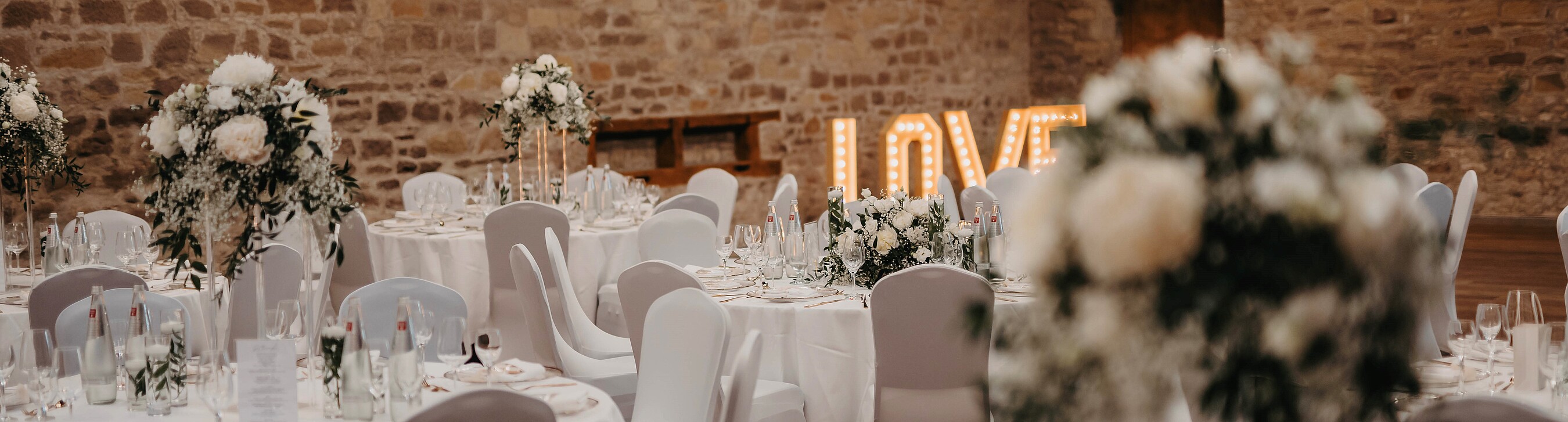 Blumenschmuck auf Tisch und „LOVE“-Schriftzug im Hintergrund bei einer Hochzeit in der Hochzeitslocation Gut Wöllried